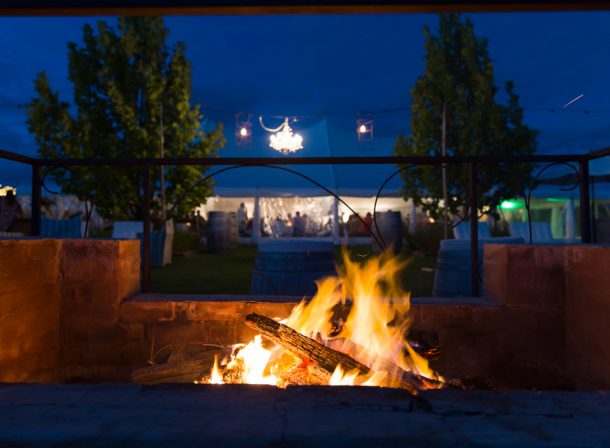 Cozy firepit illuminating the foreground, with a wedding reception in a beautifully decorated marquee in the background.