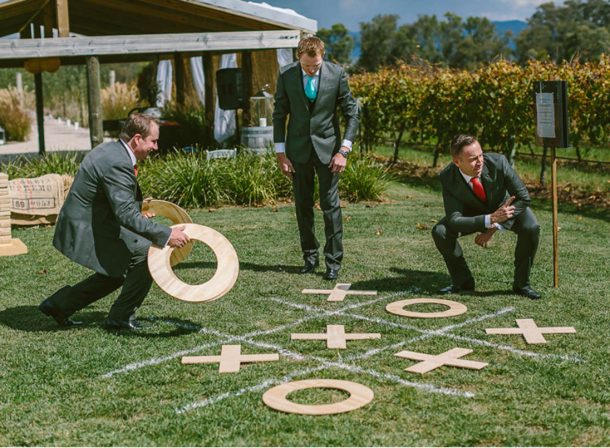 Groomsmen in dapper suits playing giant noughts and crosses on lawn.