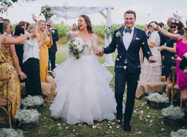 Happy couple walking joyfully down the aisle cheered on by happy guests