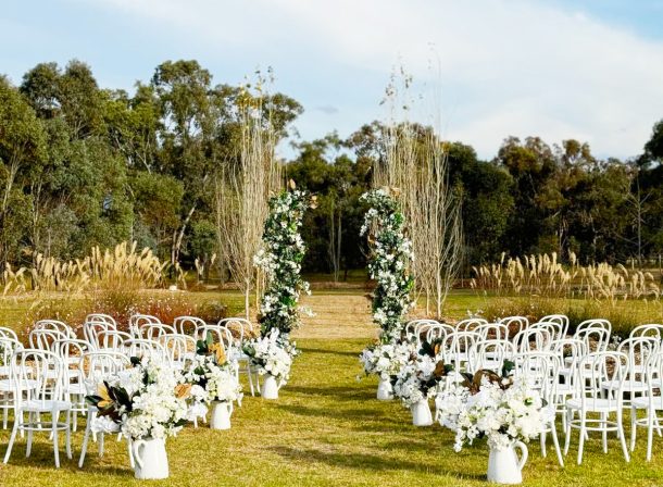 Beautiful white bentwood chairs for guests on either side of a white rose-lined aisle, facing towards an avenue of poplars where the bride will walk down to meet her groom.