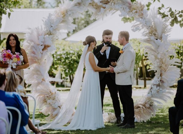 Bride and groom under an ethereal circular arch adorned with beautiful faux flowers and pampas grass